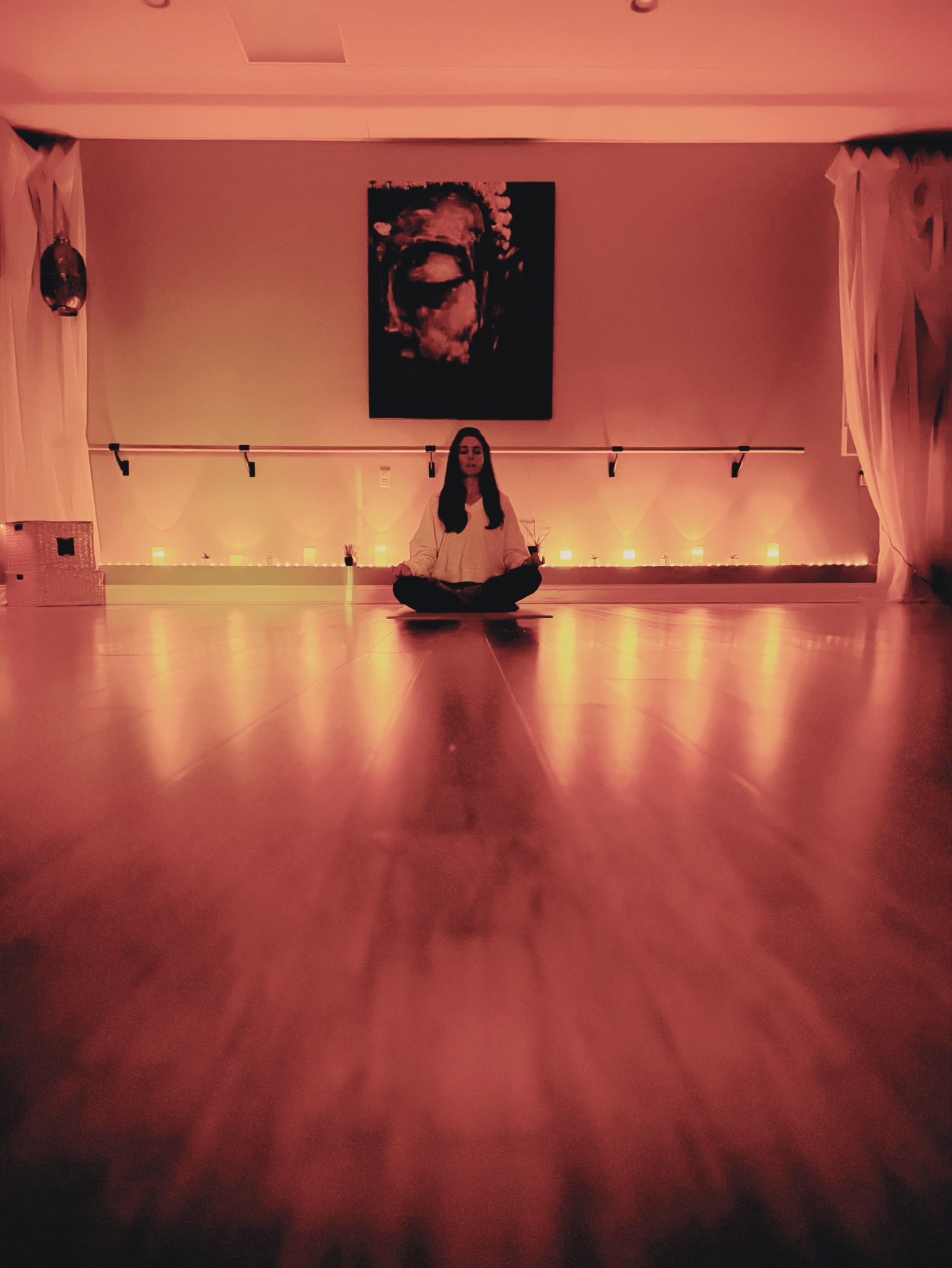 Rebekah seated in meditation at Zen Yoga & Wellness, with warm candlelight reflected across the studio floor